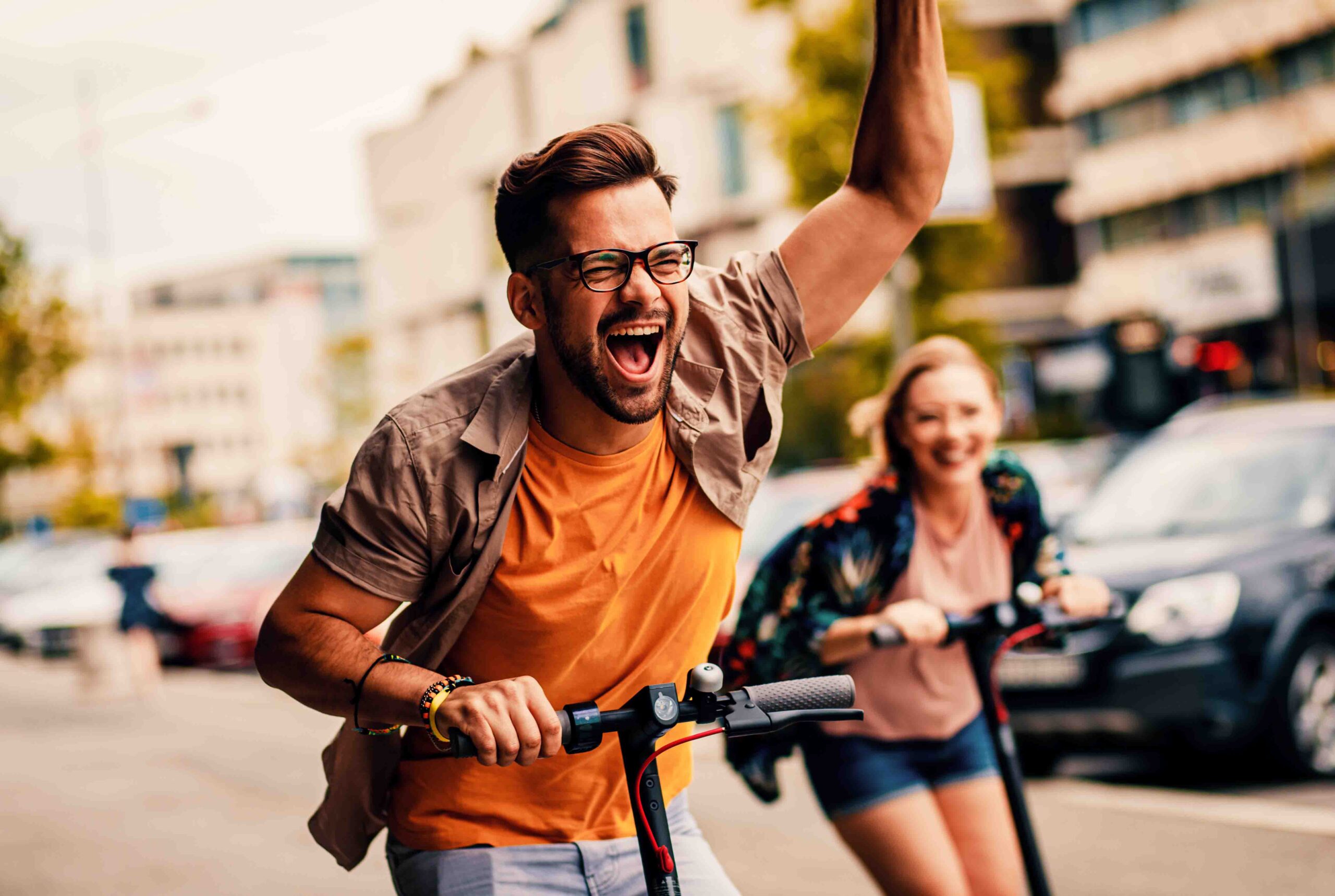 Ein Mann und eine Frau fahren mit E-Scootern durch die Stadt und haben die Roller gut versichert