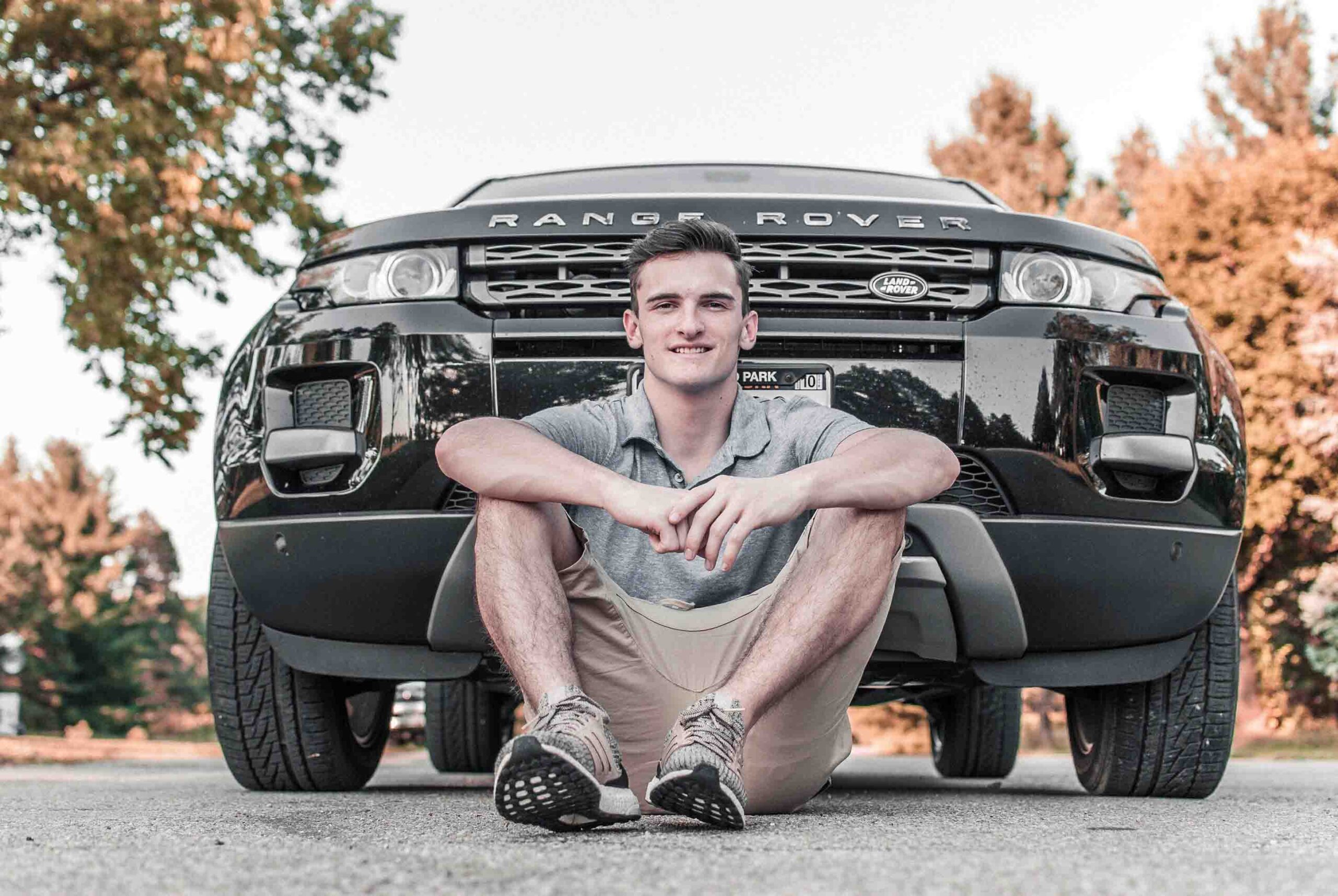 Ein junger Mann steht angelehnt an seinem Auto und hat eine gute Kfz-Versicherung