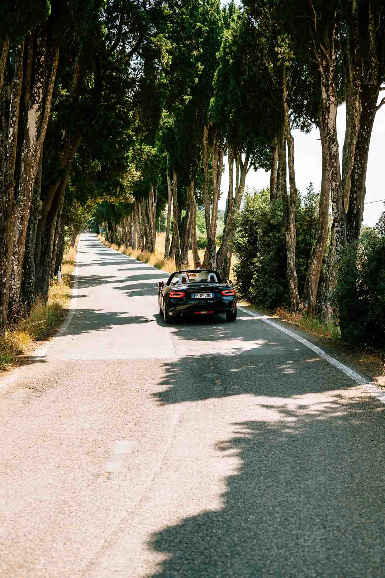 Ein Cabrio fährt eine lichtdurchflutete Landstraße entlang und ist über eine Kfz-Versicherung gut abgesichert
