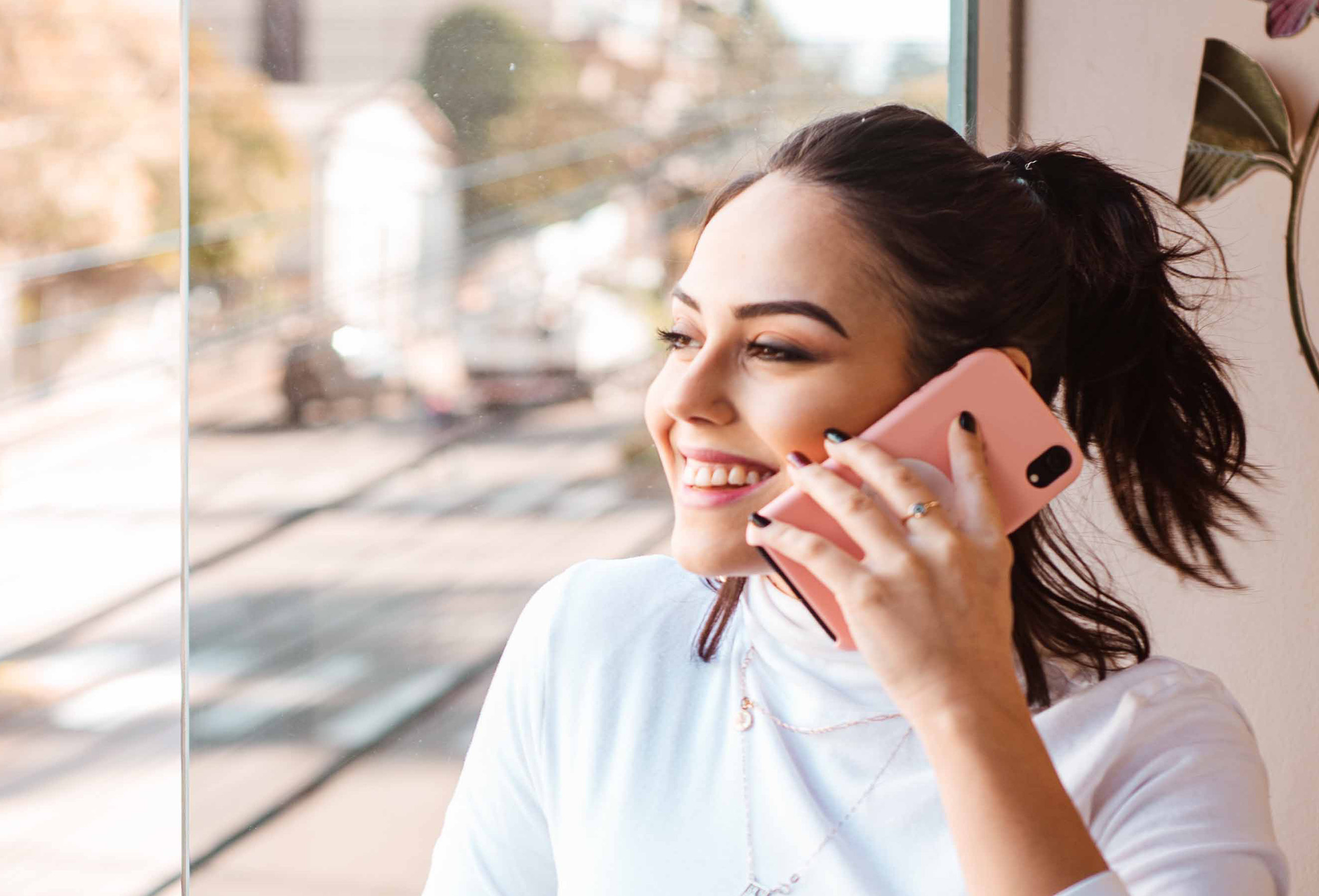 Eine junge Frau steht am Fenster und macht das Termin buchen mit Ihrem Handy
